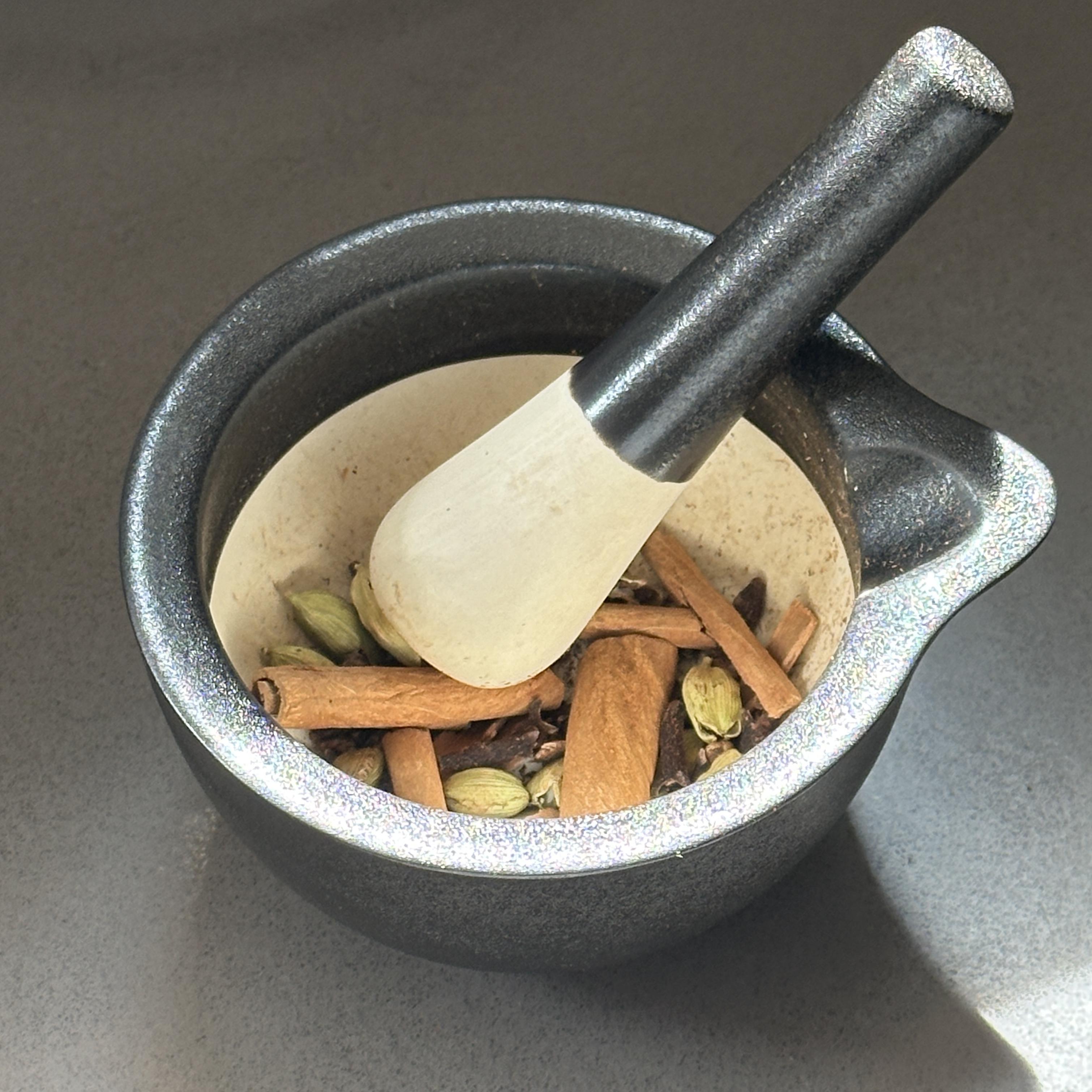 Cardamom, clove, and cinnamon being cracked fresh in a mortar and pestle
